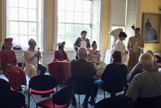 Dementia .A group of people sit in chairs and watch performers dressed in costumes from various time eras. Dementia