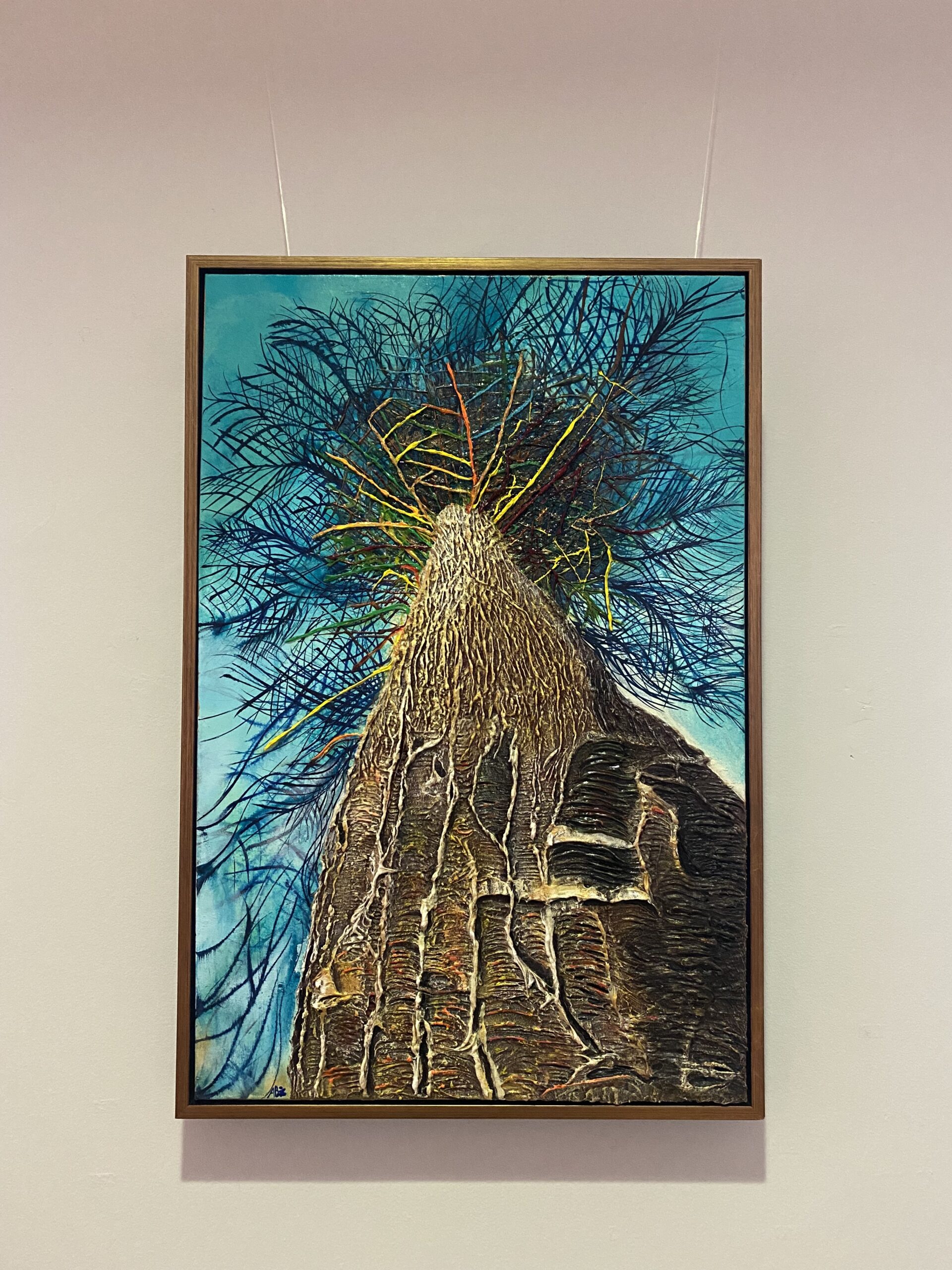 Framed painting of a textured tree trunk with colourful branches against a vivid blue sky. The artwork conveys a sense of upward growth and vibrancy.