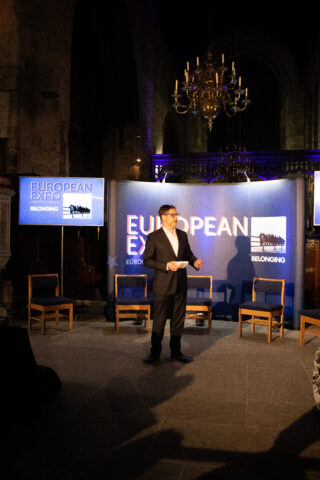 A man in a suit stands on a dimly lit stage with a 