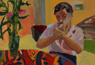 A person is lighting a cigarette in a cosy room with a warm colour palette. A vase with pink flowers and a colourful patterned tablecloth add vibrancy.