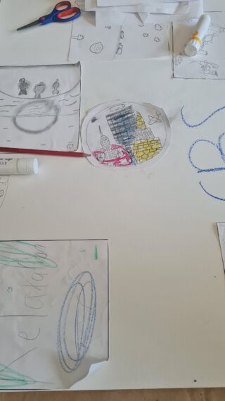 Scattered art supplies and paper with colourful drawings and sketches on a table. A pair of scissors rests nearby, evoking a creative, DIY atmosphere.