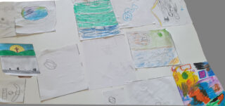 A collection of colourful children's drawings on a white table. The artworks feature bright landscapes, abstract shapes, and playful scenes, conveying creativity and joy.