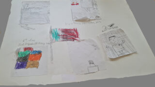 Handmade sketches and colourful paint swatches are arranged on a large sheet of light paper. The setup conveys creativity and artistic exploration.