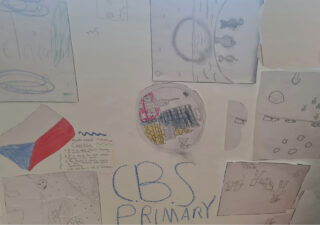 A display of children's drawings on a wall, featuring colourful and pencil-sketched shapes, symbols, and the words 