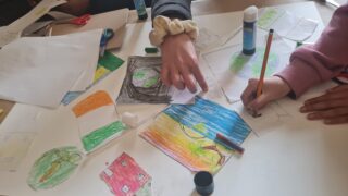 Two people work on an art project with colourful paper cut-outs, pencils, and glue on a table, creating a creative and collaborative atmosphere.