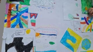 Children's colourful abstract drawings are scattered on a table. Vibrant patterns and shapes convey creativity and playfulness, with hands partially visible.