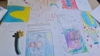 A table covered with colourful children's drawings, featuring bright landscapes, a rainbow, and a decorated wand, conveying creativity and playfulness.