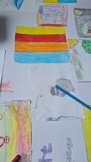 Children's colourful drawings spread on a table include a rainbow flag, abstract shapes, and a pencil, conveying creativity and playfulness.