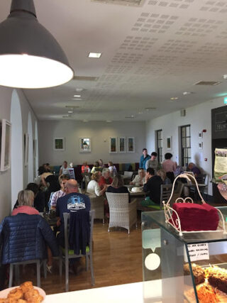A cosy Hunt café filled with people sitting at tables, enjoying conversations. The atmosphere is lively and welcoming. Baked goods are visible in the foreground.