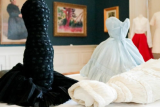 Gowns draped and folded abstractly on a museum table. Elegant textures in black, blue, and white contrast the dim-lit, art-filled room.