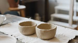Two handcrafted clay bowls with rustic, uneven edges sit on a white cloth. They rest on a wooden table, suggesting a cosy, artisanal setting.