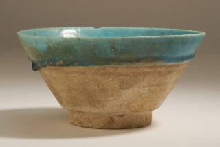 Rustic ceramic bowl with a textured, earthy brown base and a vibrant turquoise glazed rim. The contrast suggests natural beauty and handmade craftsmanship.