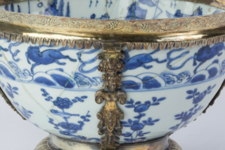 Ornate blue and white porcelain bowl with intricate floral patterns, featuring elaborate gold handles shaped like mythical figures on a gold pedestal base.