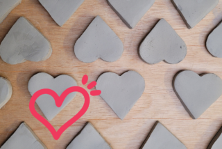 Concrete heart shapes laid on a wooden surface, evenly arranged. A pink heart sticker is in the lower left corner, adding a playful touch.