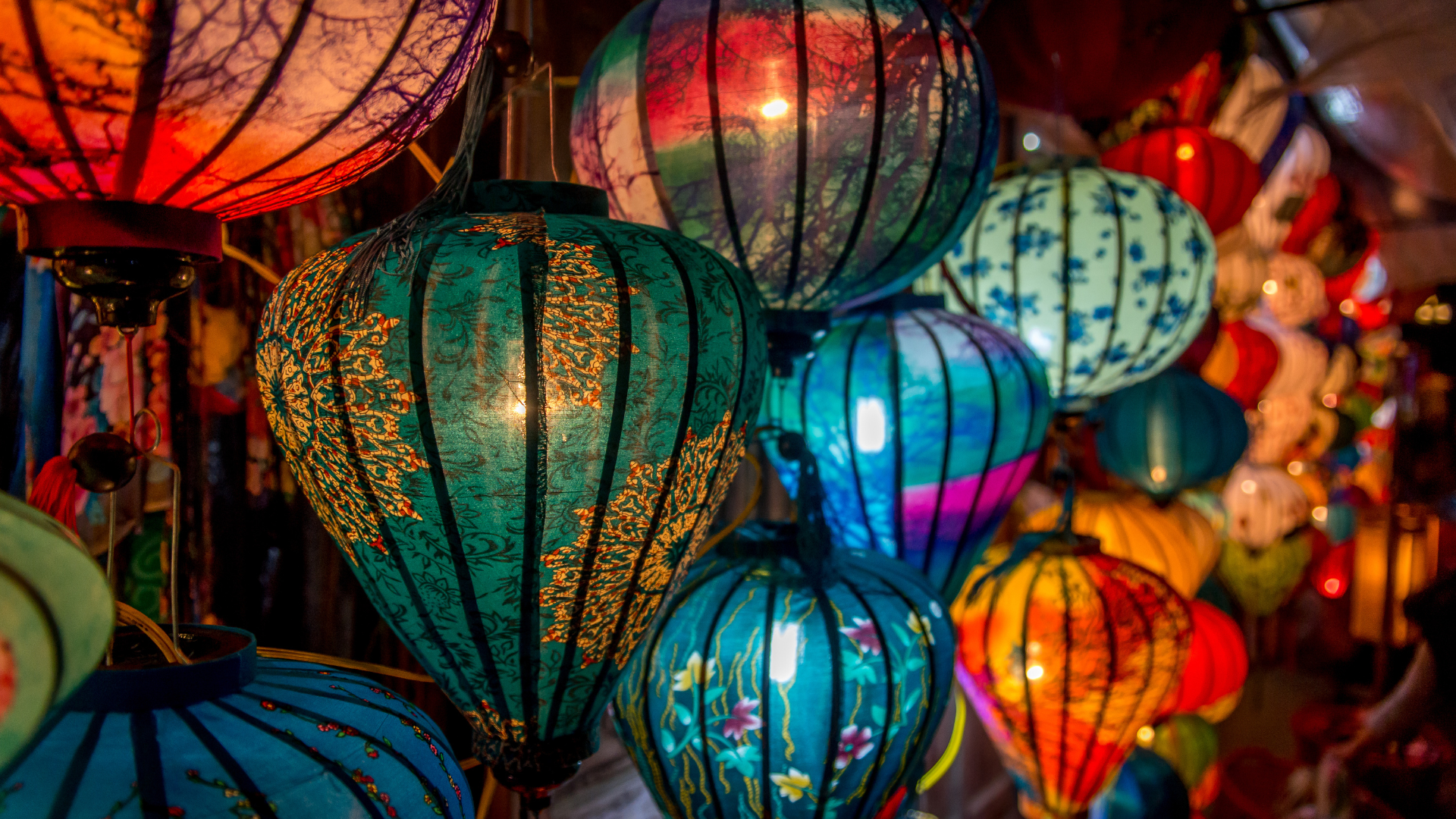 Colourful, intricately patterned lanterns hanging closely together, emitting a warm, inviting glow. The vibrant colours create a festive atmosphere.