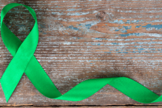 Green ribbon arranged in a loop on distressed wooden surface, symbolizing mental health awareness. The tone is calming and supportive.