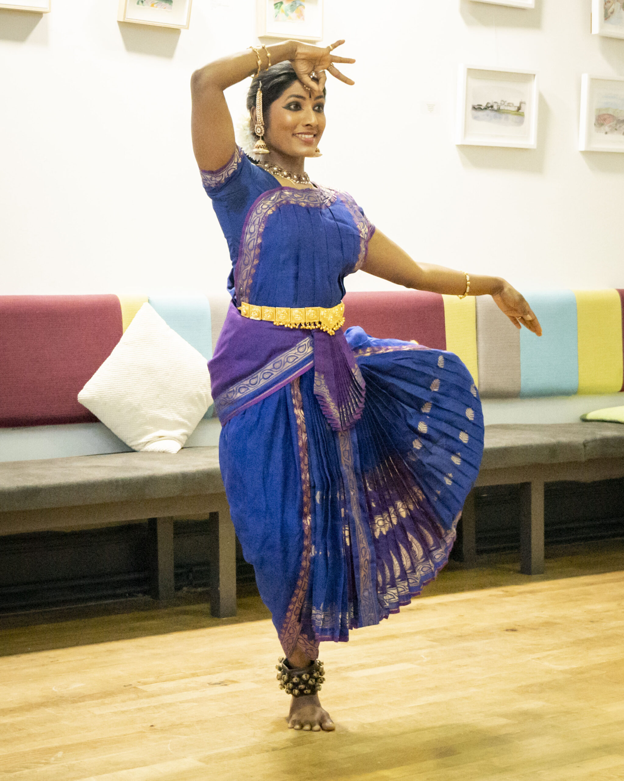 A woman performs a classical dance, wearing a vibrant blue and purple traditional costume with gold embellishments, exuding grace and concentration.