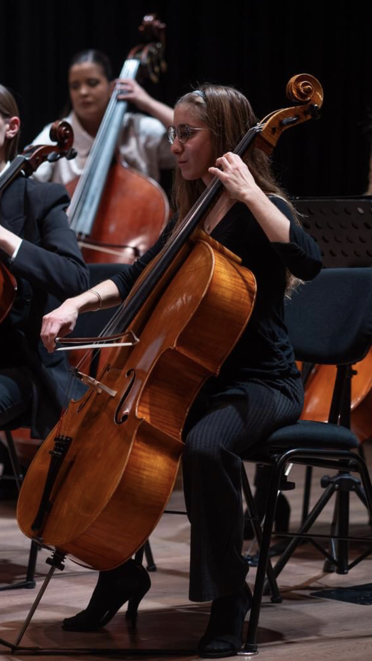 A focused musician plays the cello in an orchestra. The setting is formal, with dim lighting and a sense of concentration and harmony.