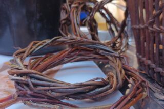 A close-up of intertwined, natural brown vines resting on a surface, with wicker baskets and a black pot in the background.