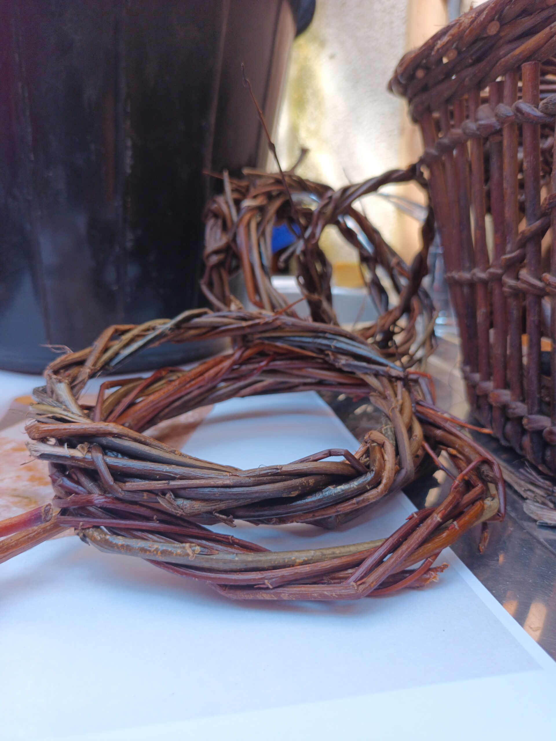 A close-up of intertwined, natural brown vines resting on a surface, with wicker baskets and a black pot in the background.