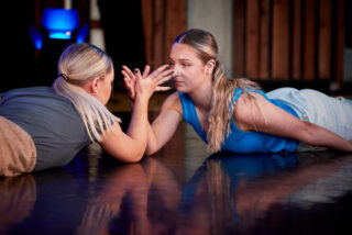 Two women engage in an intense arm-wrestling match on a polished floor, showcasing determination and focus.