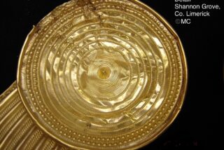 Close-up of a circular gold artifact with intricate spiral patterns from Shannon Grove, County Limerick.