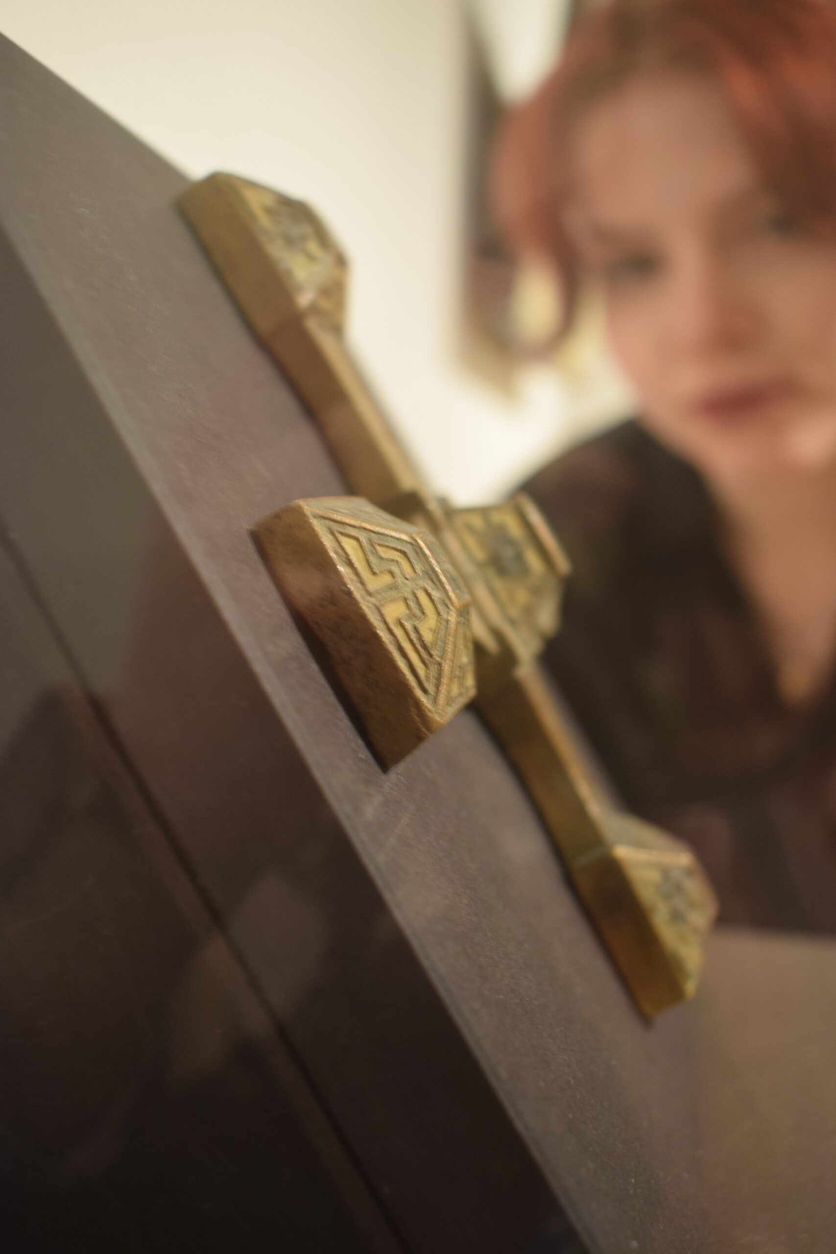 A close-up of an intricately designed golden cross on a dark background, highlighting its geometric patterns and craftsmanship.