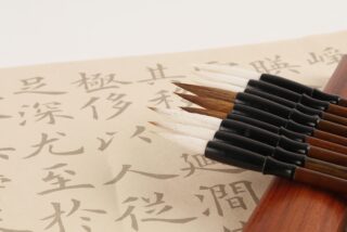 A set of calligraphy brushes rests on a sheet of paper filled with Chinese characters. The scene conveys a sense of traditional artistic practice.