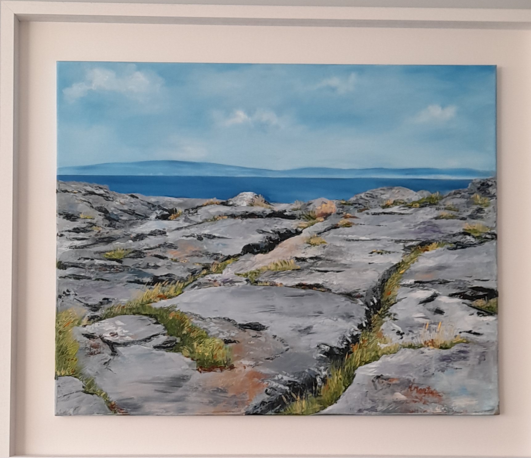 A rocky landscape painting featuring rugged stones, patches of grass, and a serene blue sea under a bright sky.