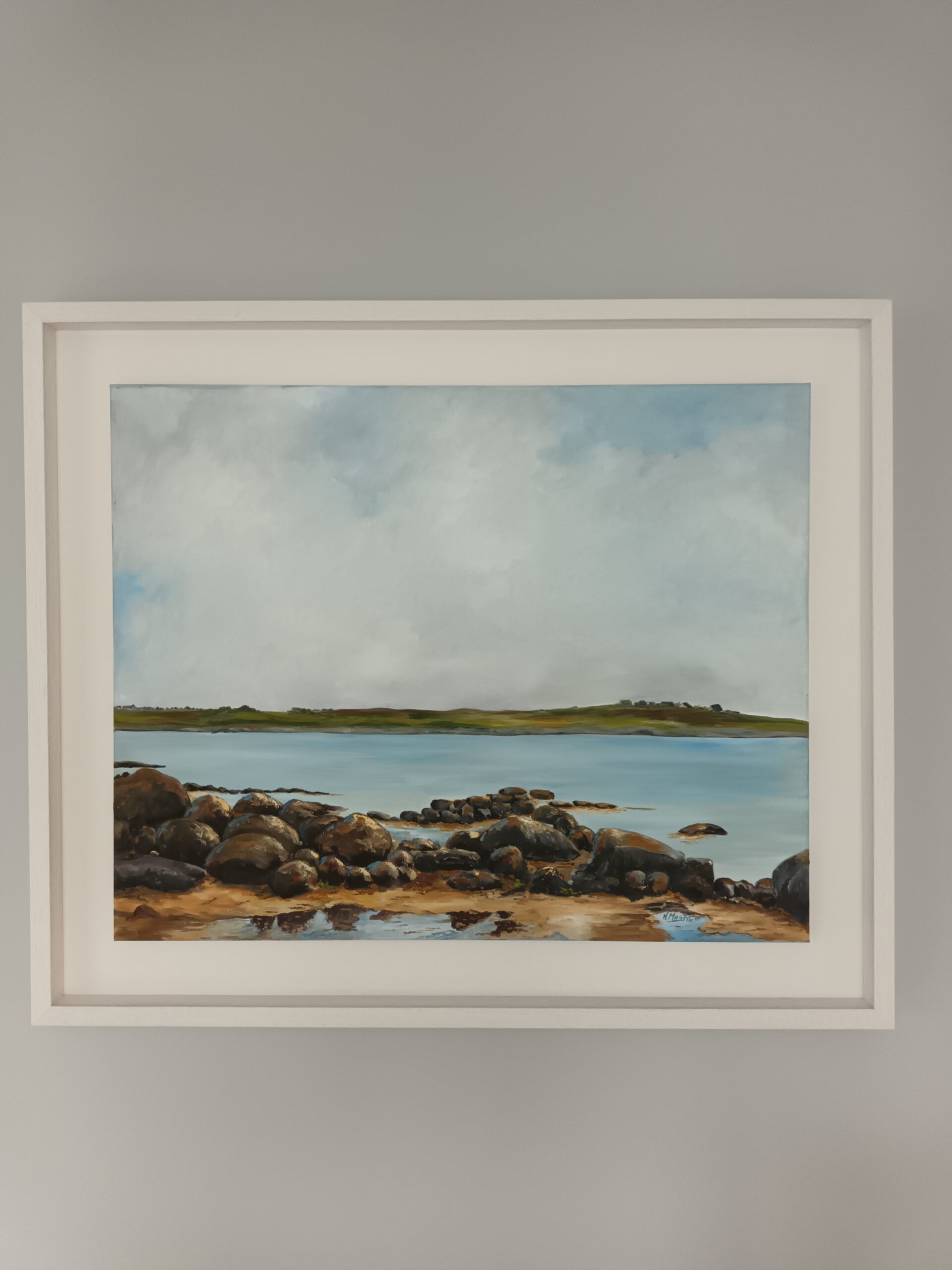 A serene landscape painting of rocky terrain leading to a calm blue sea under a clear sky, framed elegantly.