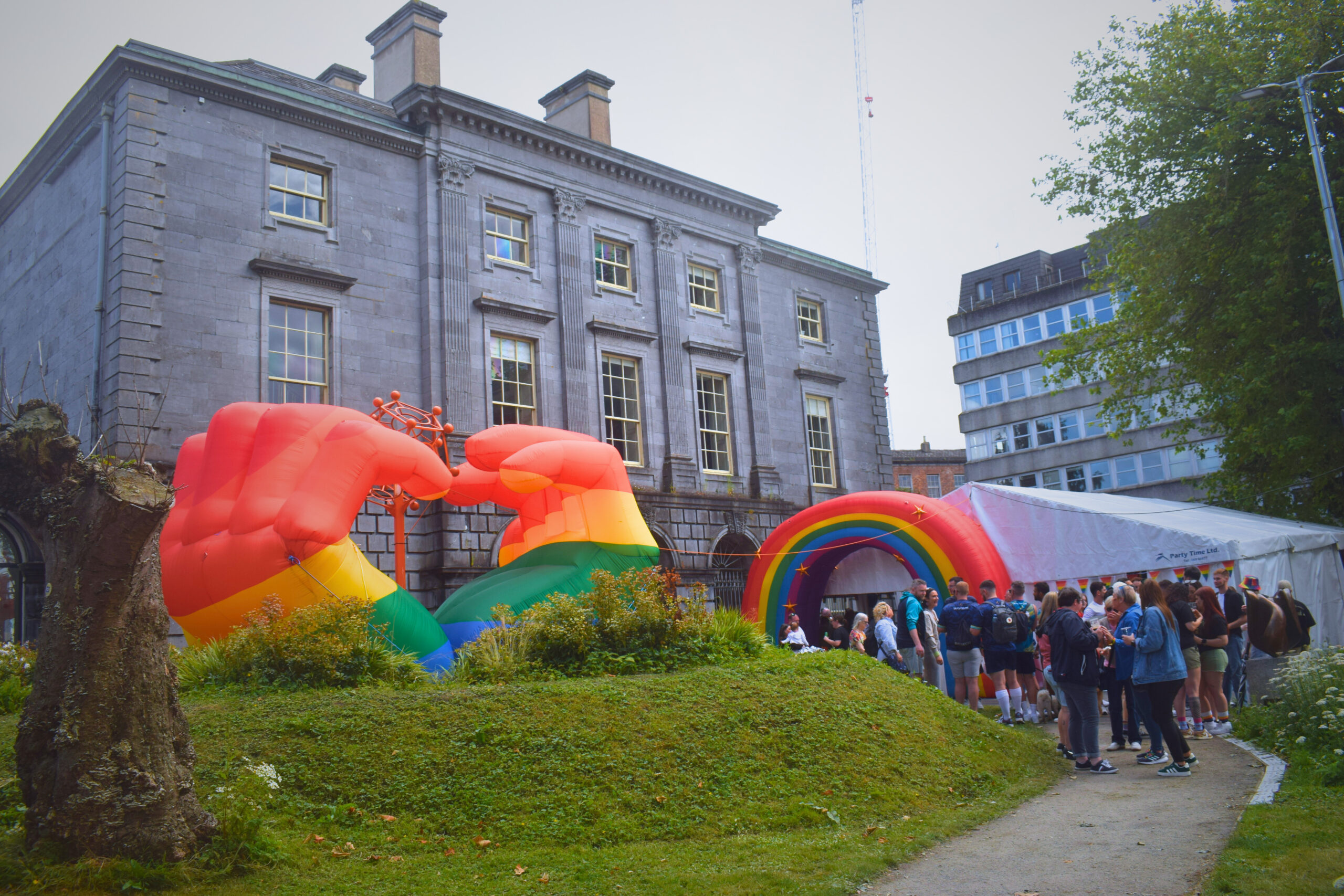 Large inflatable rainbow-colored hands and an arch are set up outside the Hunt Museum. People gather nearby, creating a festive atmosphere.