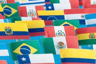 Lots of small handmade flags of latin american countries over blue background