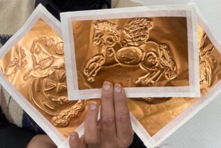 A close up of a lady holding three pieces of copper embossing artworks.