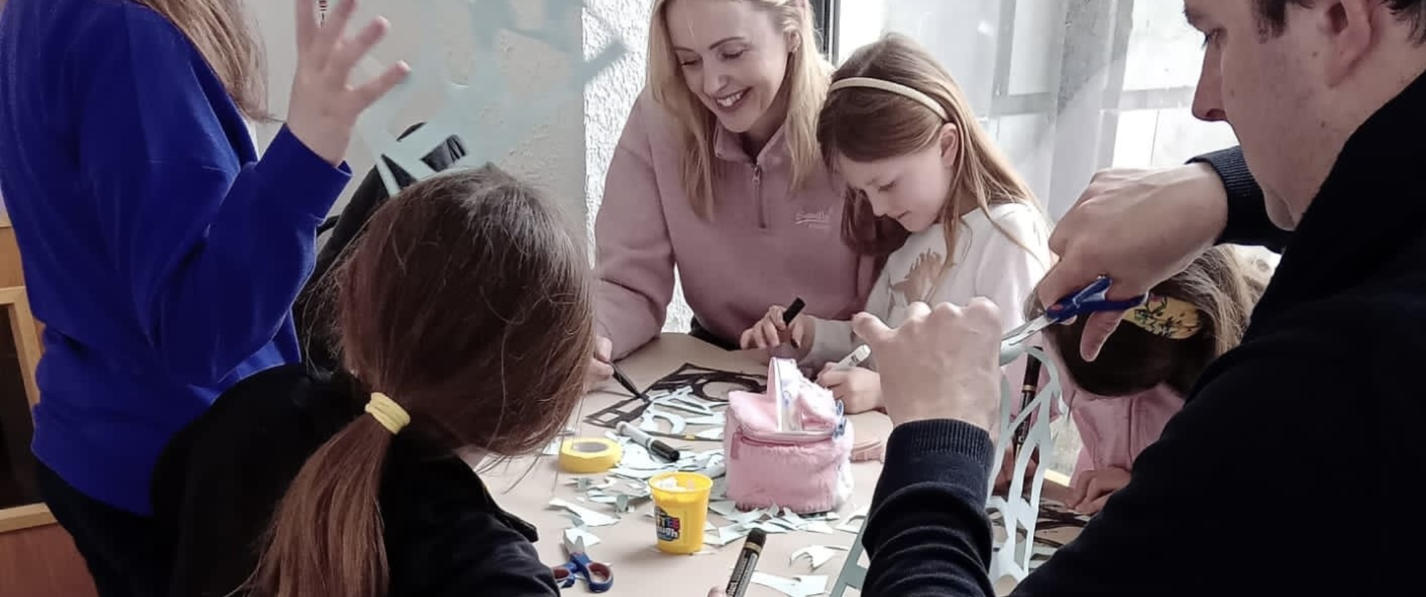 A family of a mother, children and father making paper crafts at a table.