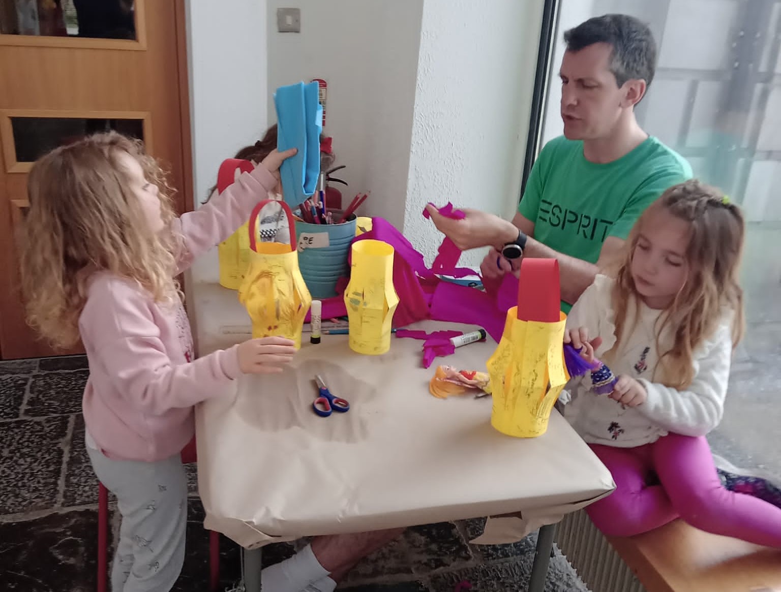 A family of children and father making paper crafts at a table.